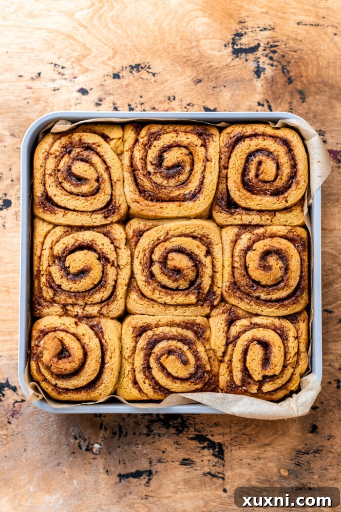 Freshly baked gluten-free pumpkin cinnamon rolls, golden brown and glistening, cooling slightly in their baking dish before frosting.
