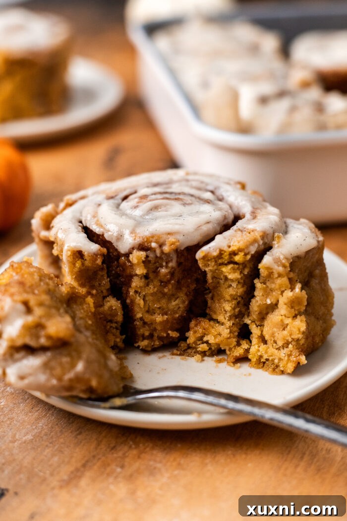 A close-up of a bitten gluten-free pumpkin cinnamon roll, revealing its soft, fluffy interior and generous swirls of spiced filling.