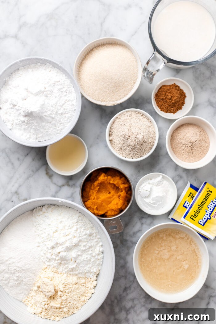 Various gluten-free cinnamon roll ingredients, including flours, spices, and wet ingredients, artfully arranged on a marble surface, ready for preparation.
