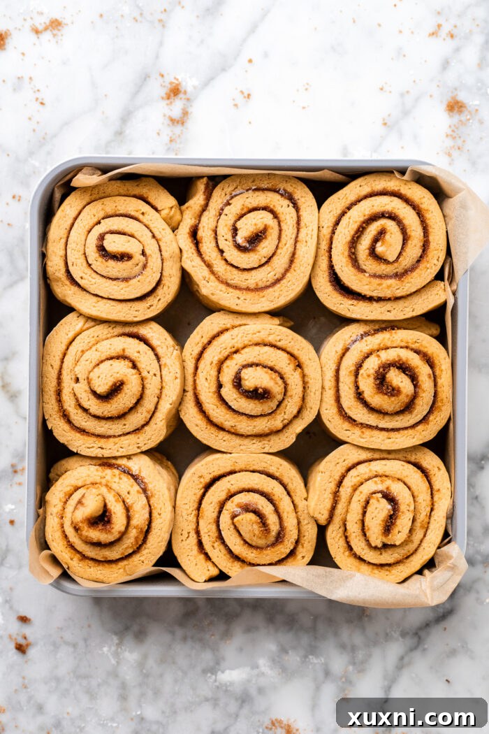 Unbaked gluten-free pumpkin cinnamon rolls nestled in a baking dish, perfectly formed and ready to rise before baking.