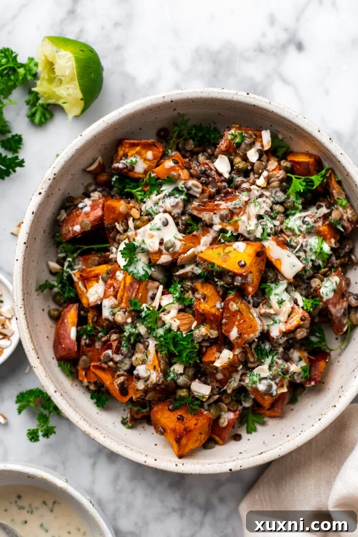 Tossed sweet potato lentil salad in a bowl, topped with almonds, capers, and fresh parsley