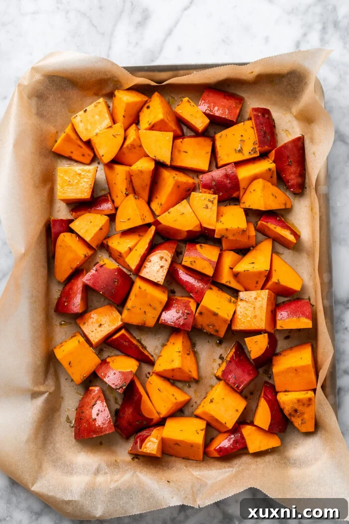 Sweet potato wedges seasoned with olive oil, cumin, and Italian seasoning on a baking sheet before baking