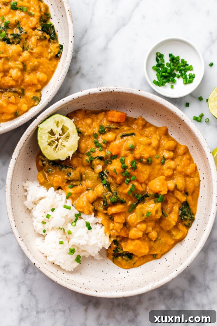 Creamy Peanut Butter Sweet Potato Curry with Chickpeas and Kale 11 A serving of sweet potato curry with white rice in a bowl, garnished with fresh cilantro and a lime wedge.