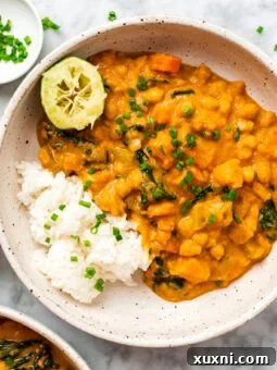 A bowl of rich sweet potato curry with a lime wedge, highlighting the dish's vibrant colors.