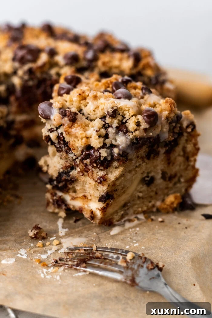 A close-up of a slice of vegan chocolate chip coffee cake with a bite taken out, highlighting its rich textures, melty chocolate, and creamy swirl.
