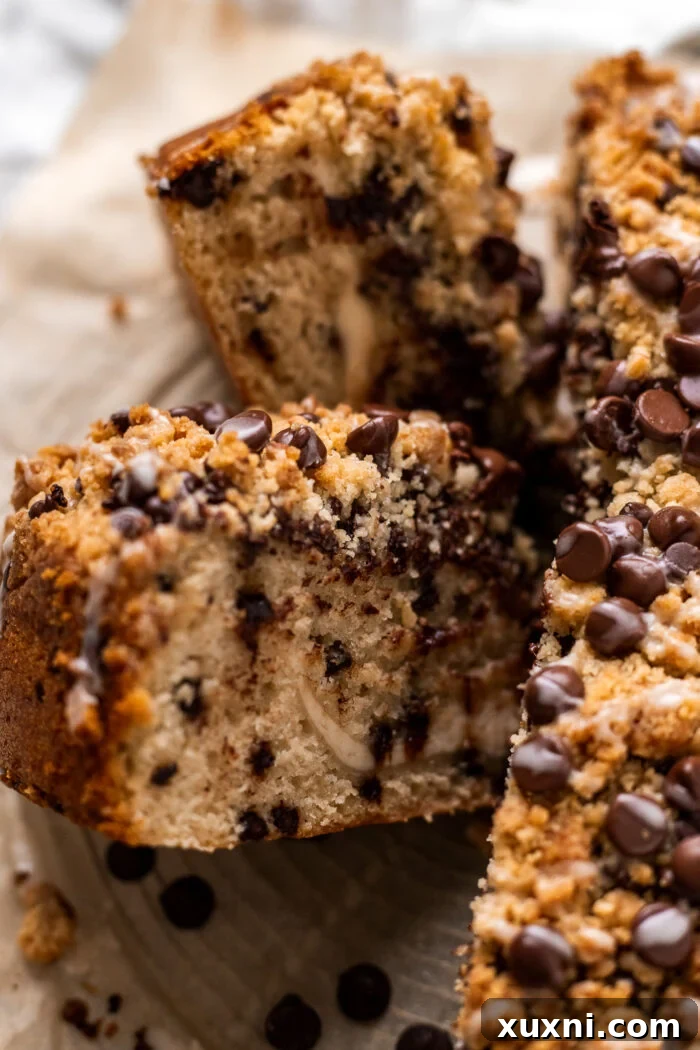 A freshly baked vegan chocolate chip coffee cake, expertly sliced, rests on parchment paper, revealing its moist layers and a rich cream cheese swirl.