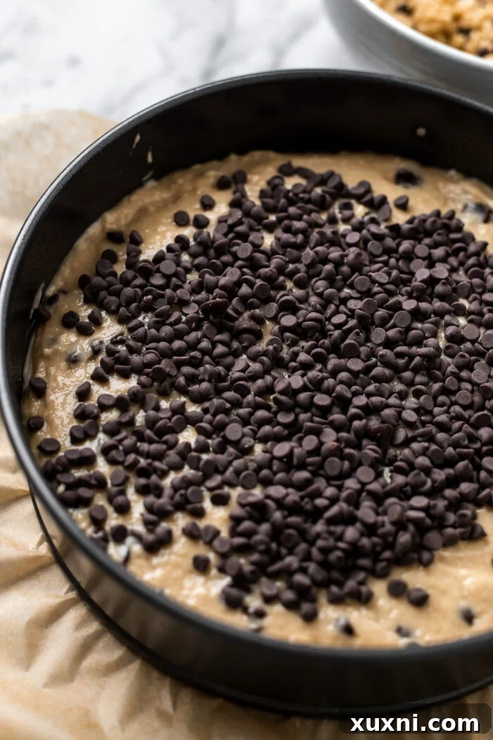 The second layer of coffee cake batter being poured over the cream cheese swirl, followed by an additional sprinkle of chocolate chips, preparing for the crumble topping.