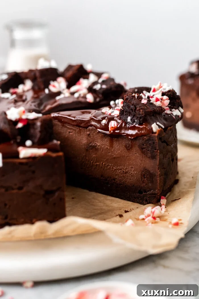 Sliced vegan chocolate peppermint brownie cheesecake on a white plate, showcasing its layers of brownie base, creamy cheesecake, and festive toppings.