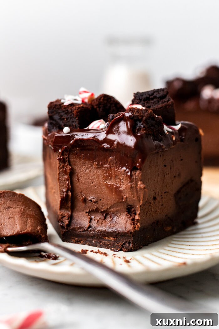 A slice of vegan chocolate peppermint brownie cheesecake on a plate, with a bite taken, showing the rich layers and internal brownie pieces.