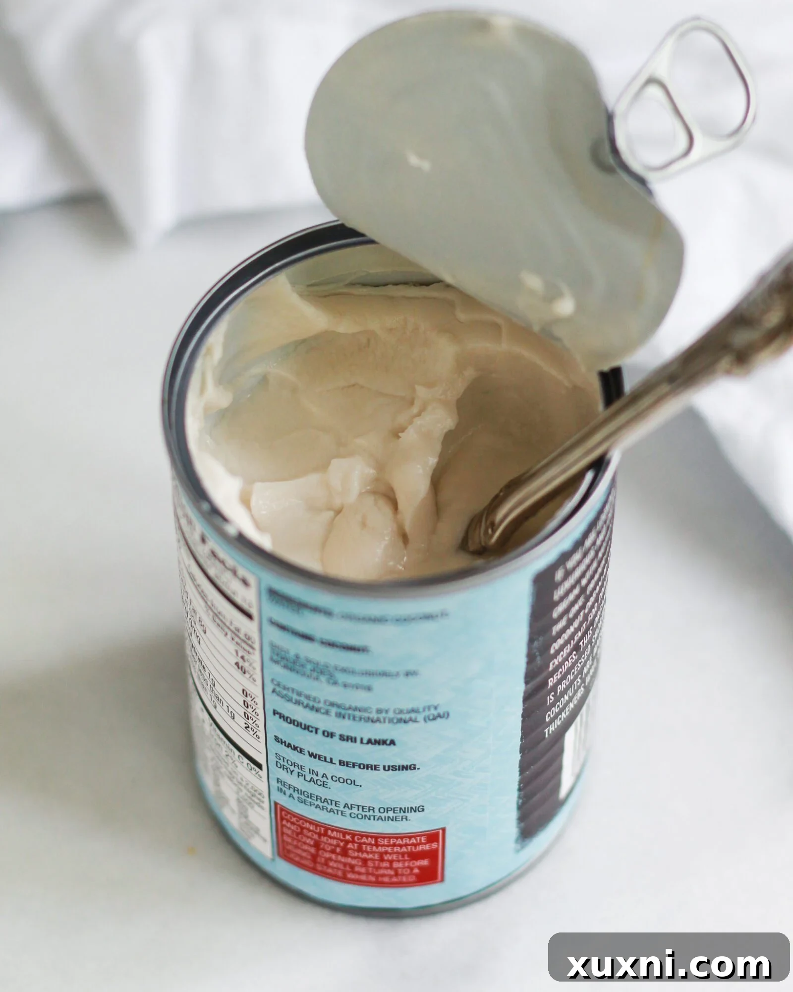 An opened can of rich coconut cream, showcasing its thick and opaque texture, ready to be used in a delicious vegan recipe.