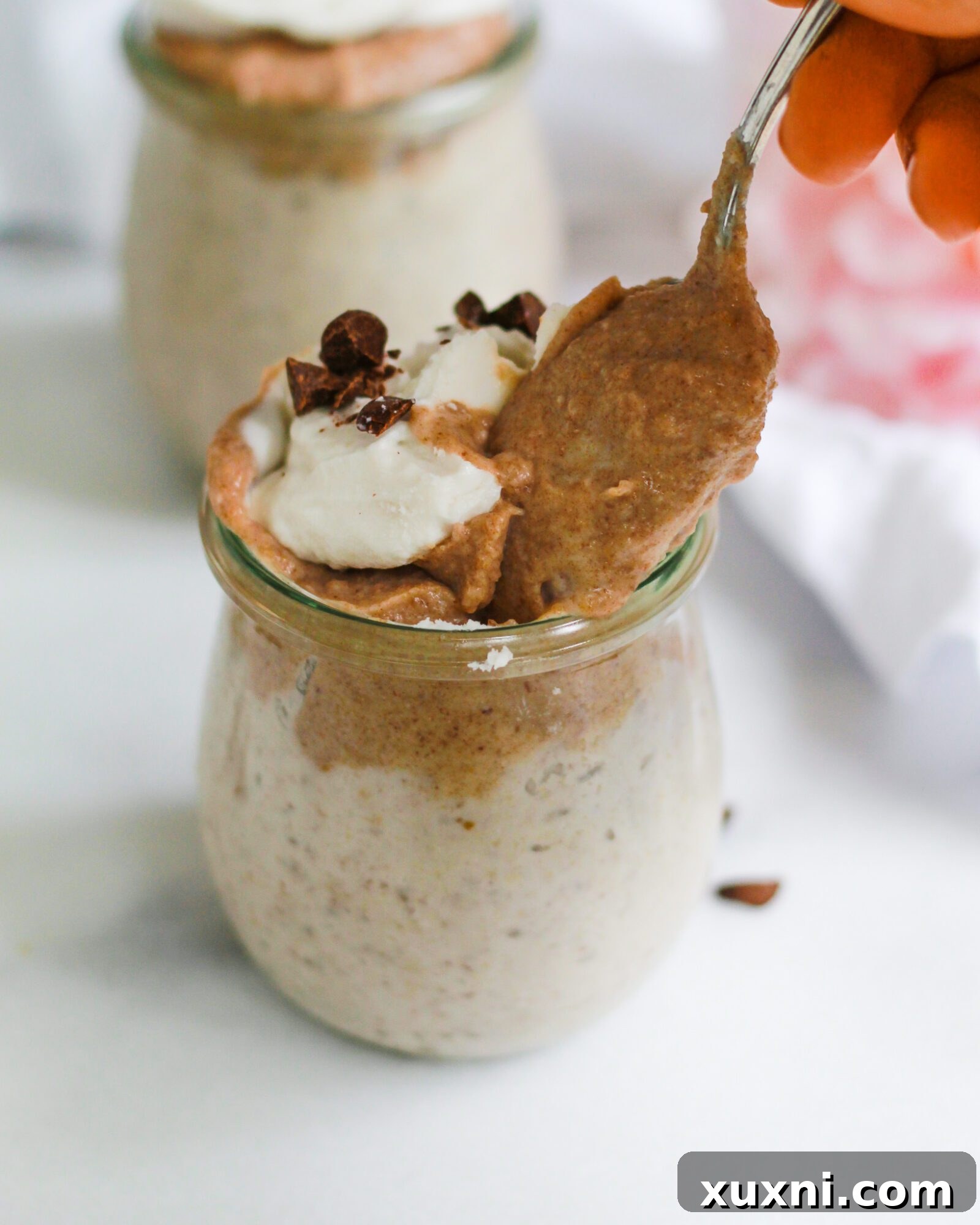 A spoon delicately enters a jar of vegan butterscotch pudding, ready to scoop out a delicious mouthful.