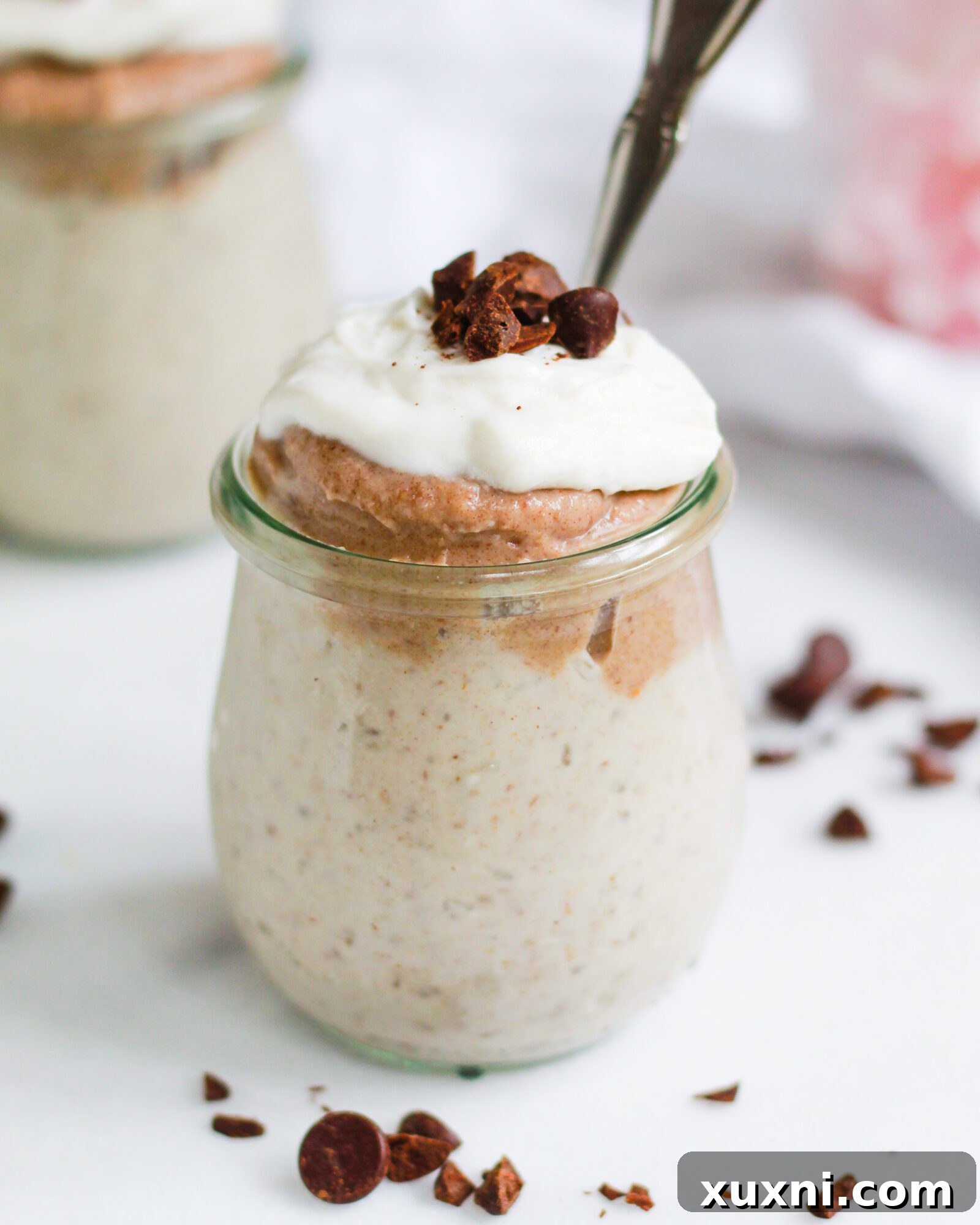 A beautifully presented jar of vegan butterscotch pudding, elegantly topped with a swirl of delicate coconut whipped cream, inviting indulgence.