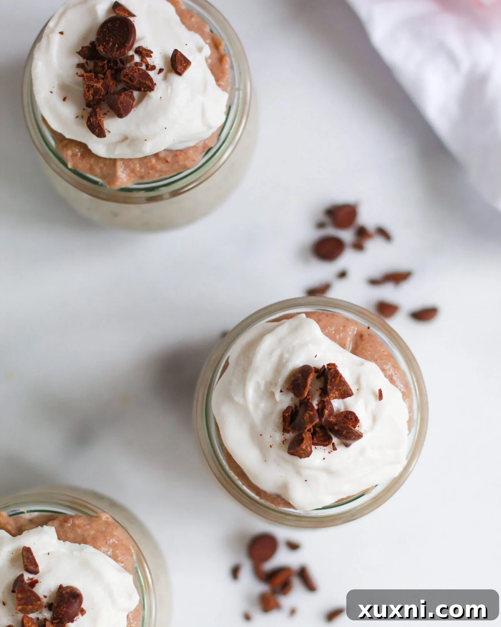 An inviting overhead view of multiple jars filled with rich vegan butterscotch pudding, each adorned with a generous dollop of coconut whipped cream.