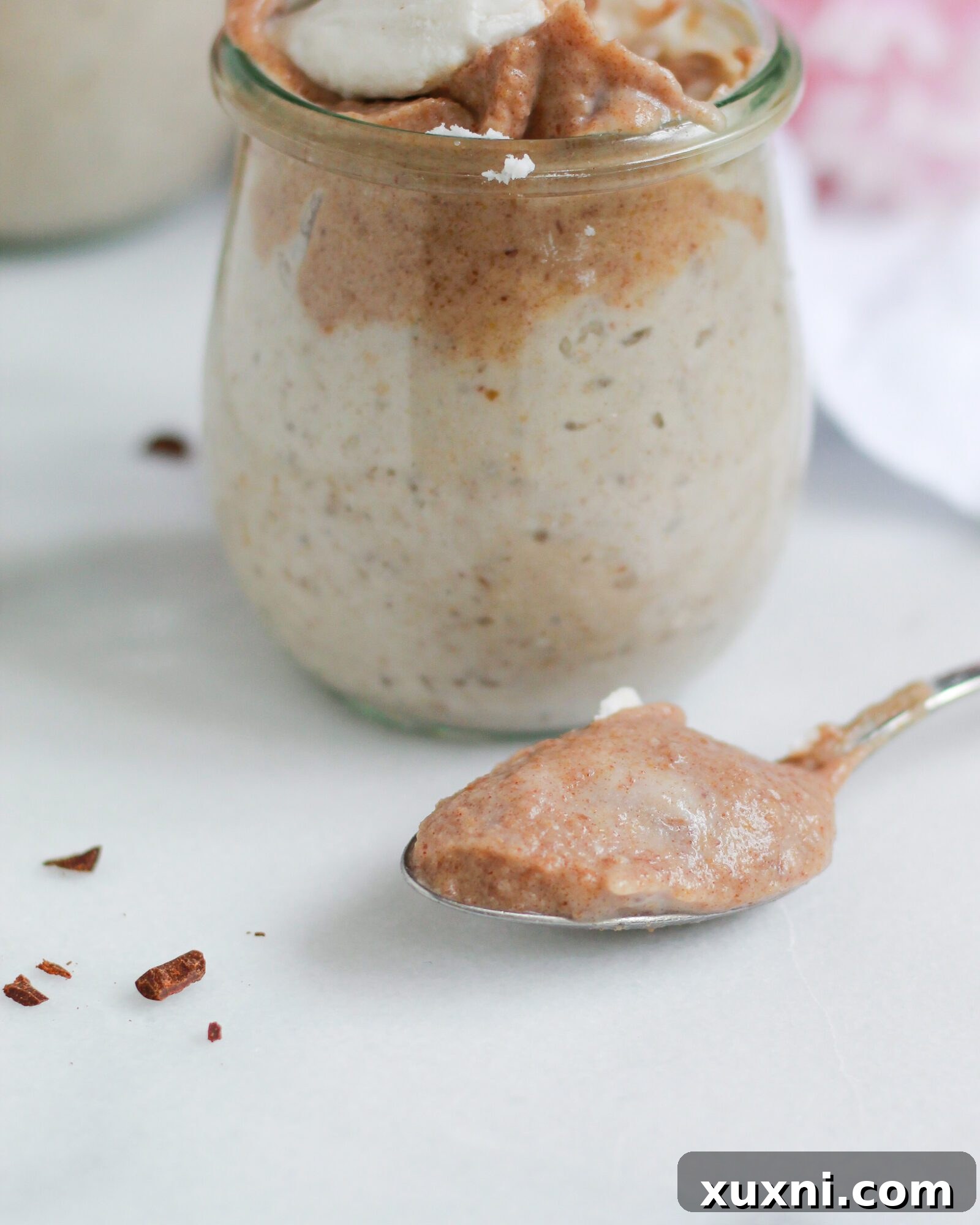 A spoon gracefully lifts a creamy dollop of vegan butterscotch pudding from a glass, highlighting its smooth and inviting texture.