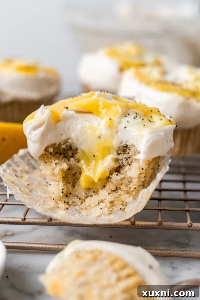 A partially eaten vegan lemon cupcake reveals its soft, moist interior and the creamy lemon curd filling, resting on a cooling rack.