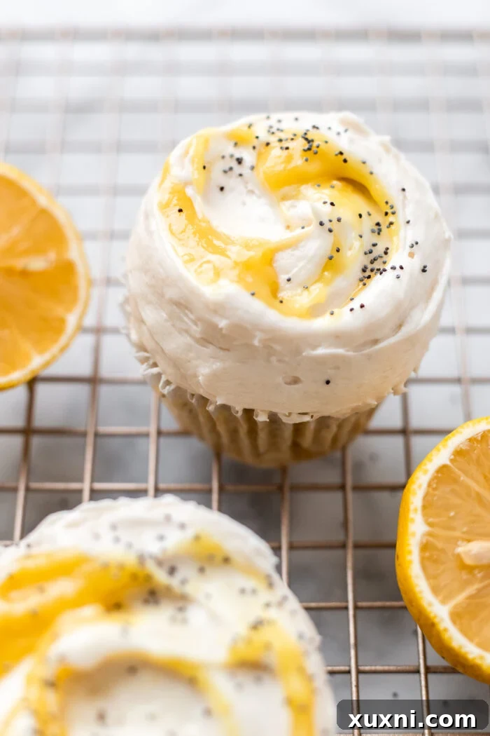 Freshly baked vegan lemon cupcakes topped with a golden dairy-free lemon curd, garnished with zest and poppy seeds, alongside fresh lemons on a cooling rack.