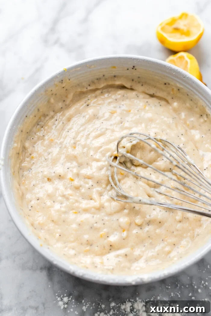 Thick, yellow vegan lemon cupcake batter ready for baking, in a mixing bowl with a whisk resting on the side.