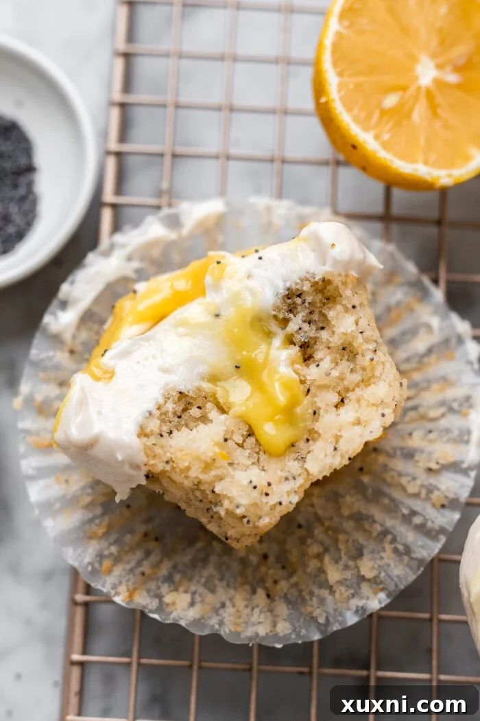 A close-up of a partially eaten vegan lemon poppy seed cupcake, revealing the bright yellow lemon curd filling and the soft, fluffy crumb.