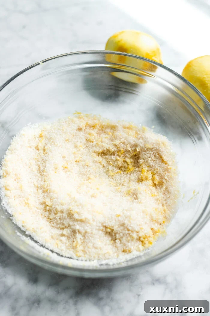 Sugar and lemon zest being rubbed together in a bowl to release lemon oils.