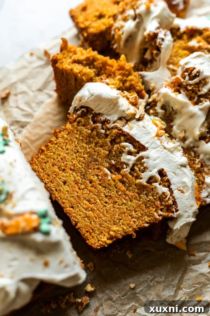 Sliced vegan carrot cake loaf on parchment paper, revealing its moist crumb and rich frosting.