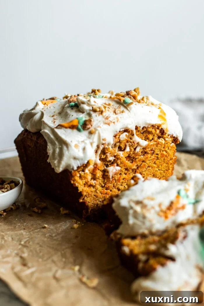 A perfectly sliced vegan carrot cake loaf, showing its soft interior and thick layer of cream cheese frosting.