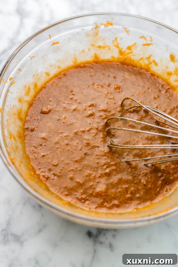 Mixing the wet ingredients for the carrot cake loaf batter in a large bowl.