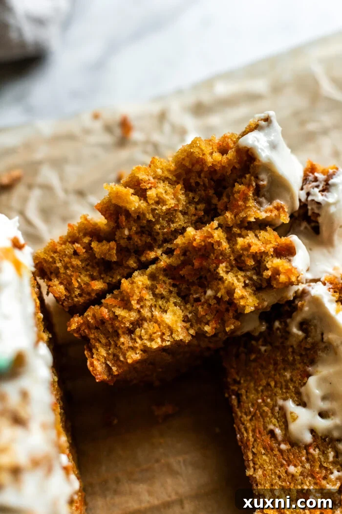 A slice of vegan carrot cake loaf topped with piped frosting carrots and crushed nuts.
