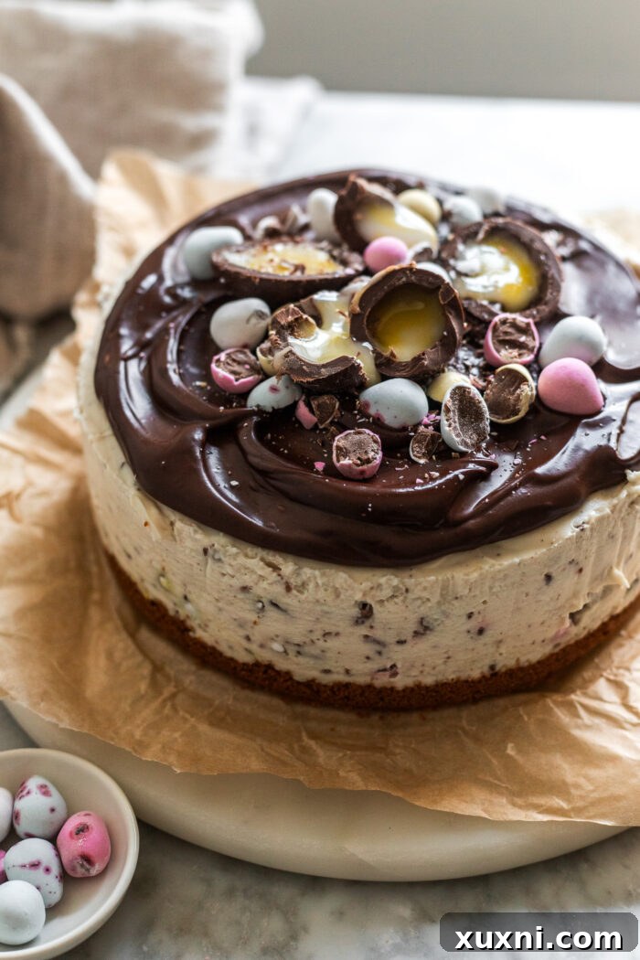 A whole no-bake Easter egg cheesecake, garnished with candies and chocolate ganache, on a serving slab