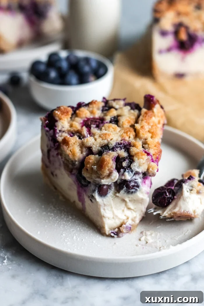 A delicious slice of vegan blueberry crumble cheesecake on a plate, with a bite taken out, revealing its creamy texture and blueberry layers.