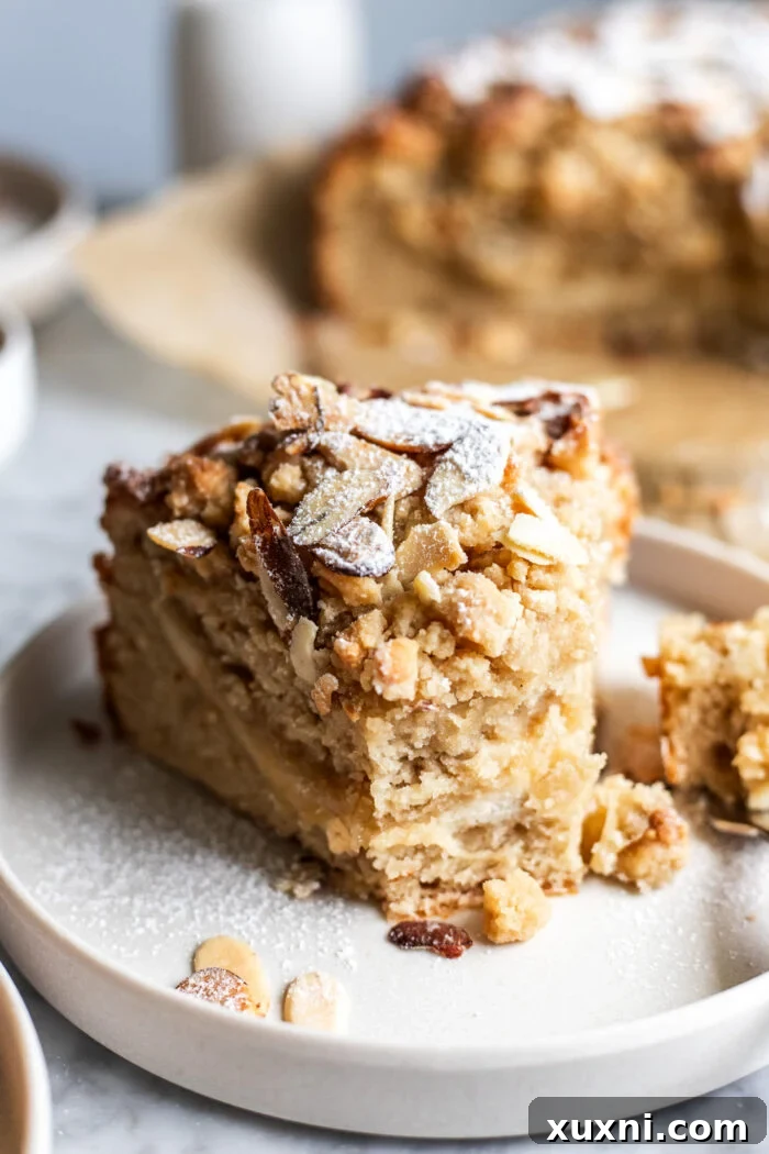 Slice of moist vegan almond coffee cake on a white plate, showcasing the creamy filling and crunchy topping.