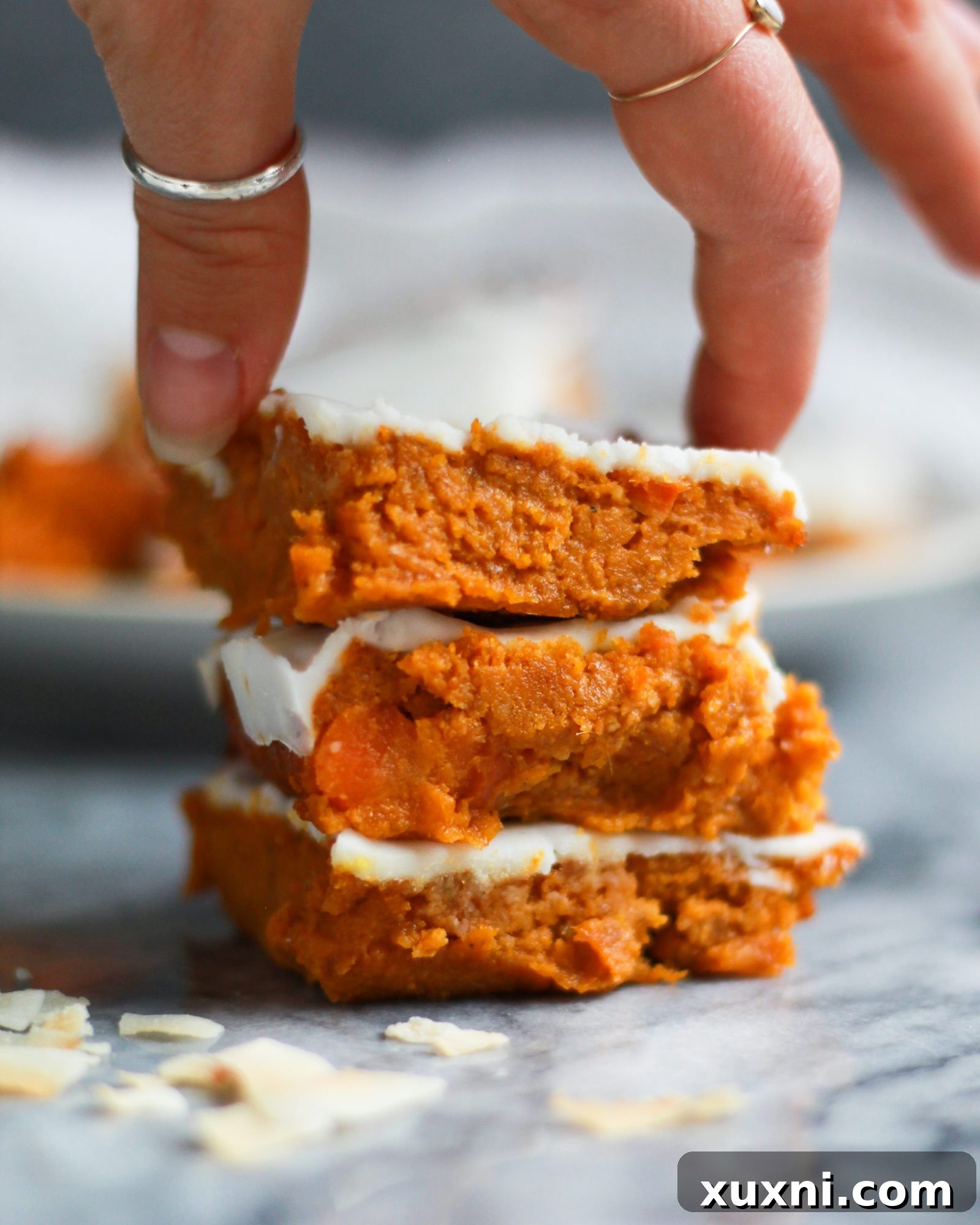 A stack of paleo vegan carrot cake bars, with a hand reaching for one, illustrating their irresistible appeal.