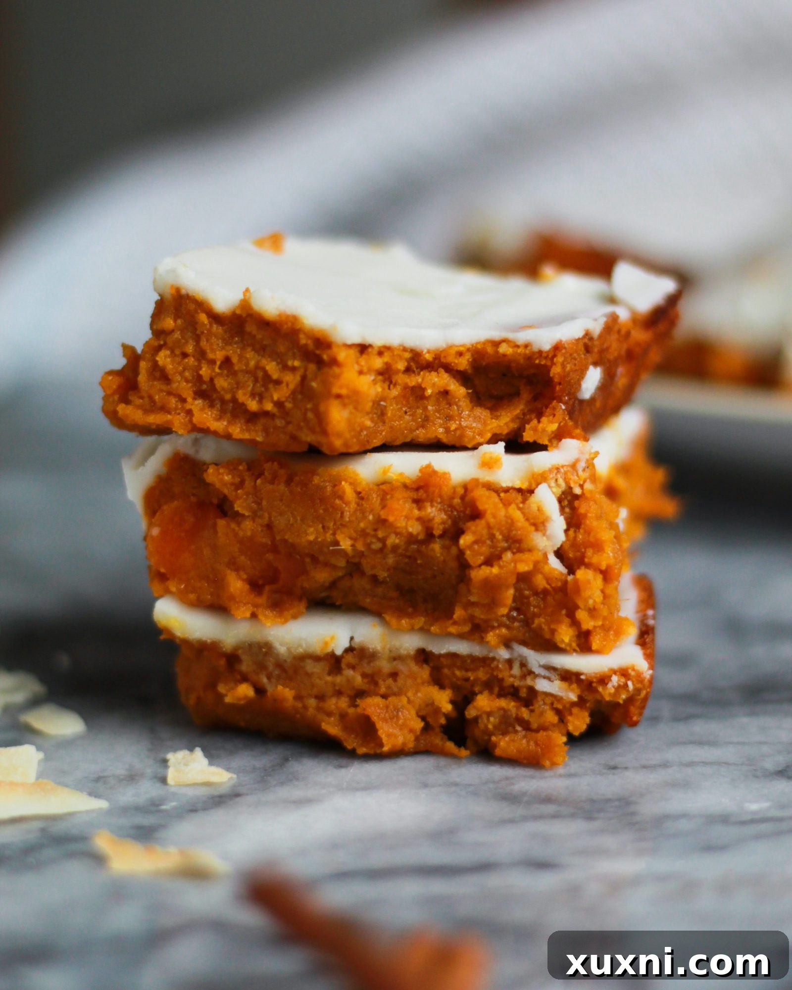 Close-up of a paleo vegan carrot cake bar with a bite taken out, showing its moist interior and delicious frosting.
