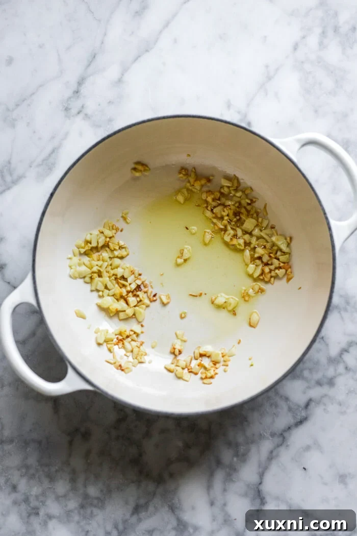 Minced garlic cloves sizzling in a pot with olive oil, creating an aromatic base for the tomato sauce.
