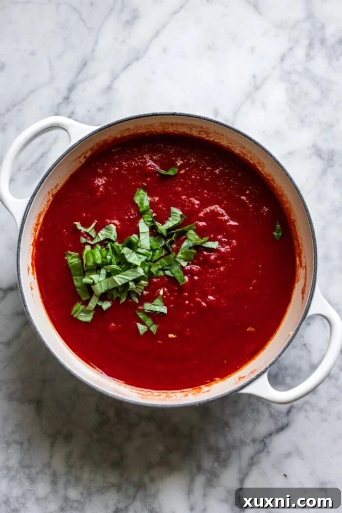 Crushed pomodorini tomatoes and fresh basil being stirred into the sautéed garlic in a pot, forming the rich sauce.