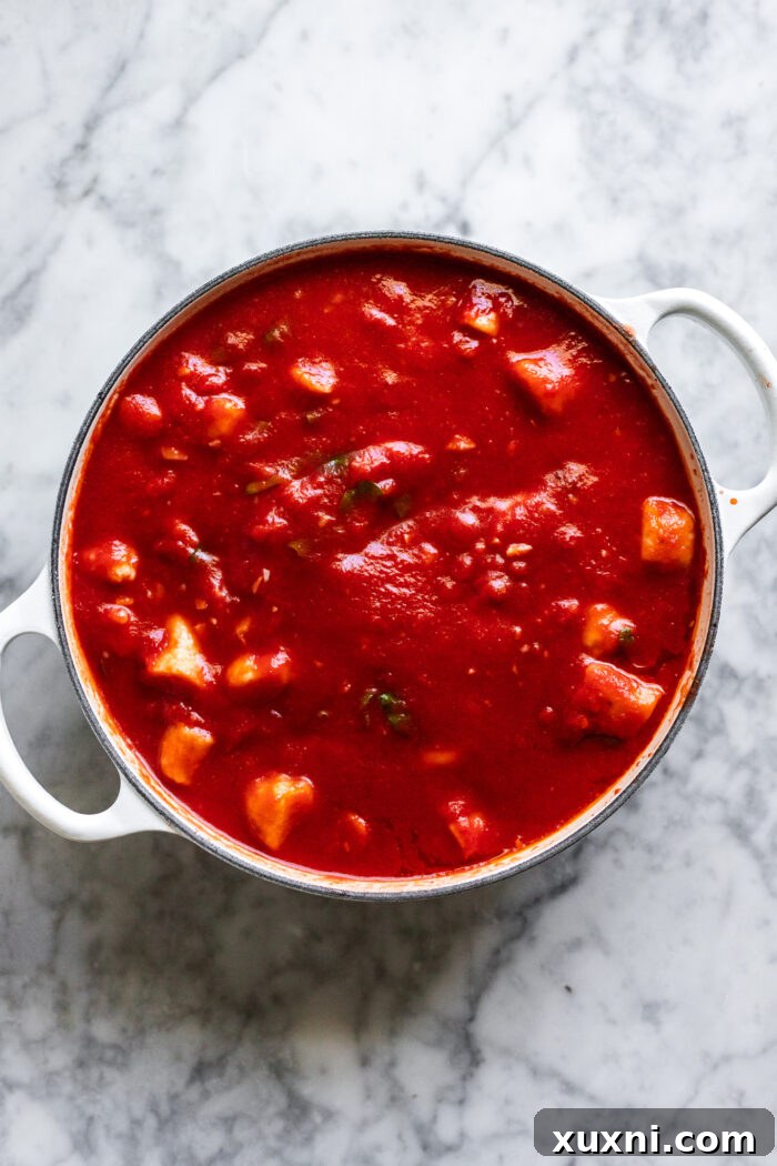 Cooked gnocchi being gently tossed with the simmering pomodorino sauce in a large pot, ensuring each piece is coated.