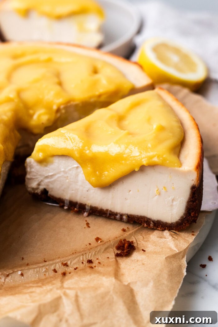 A slice of vegan lemon cheesecake topped with a generous layer of lemon curd, served on a marble plate.