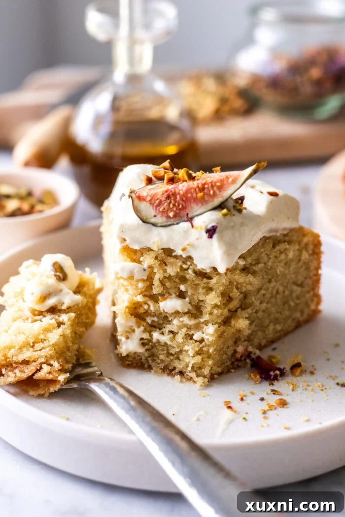 A close-up of a slice of vegan olive oil cake with a bite taken out, revealing its moist interior and creamy topping.