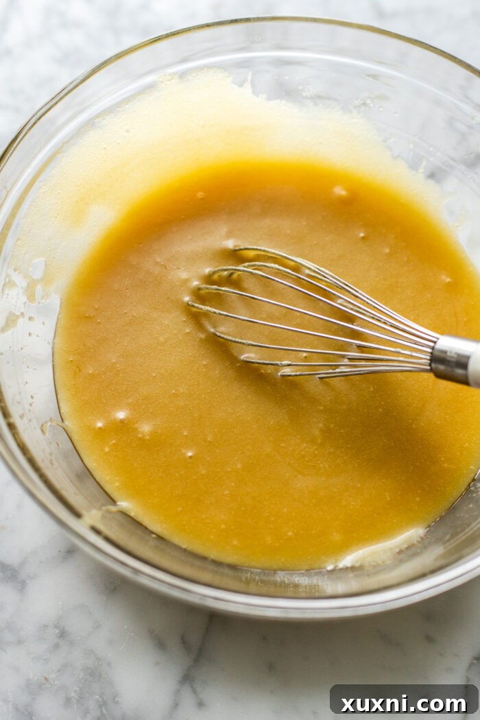 A hand whisking ingredients in a bowl, showing the process of making vegan olive oil cake batter.