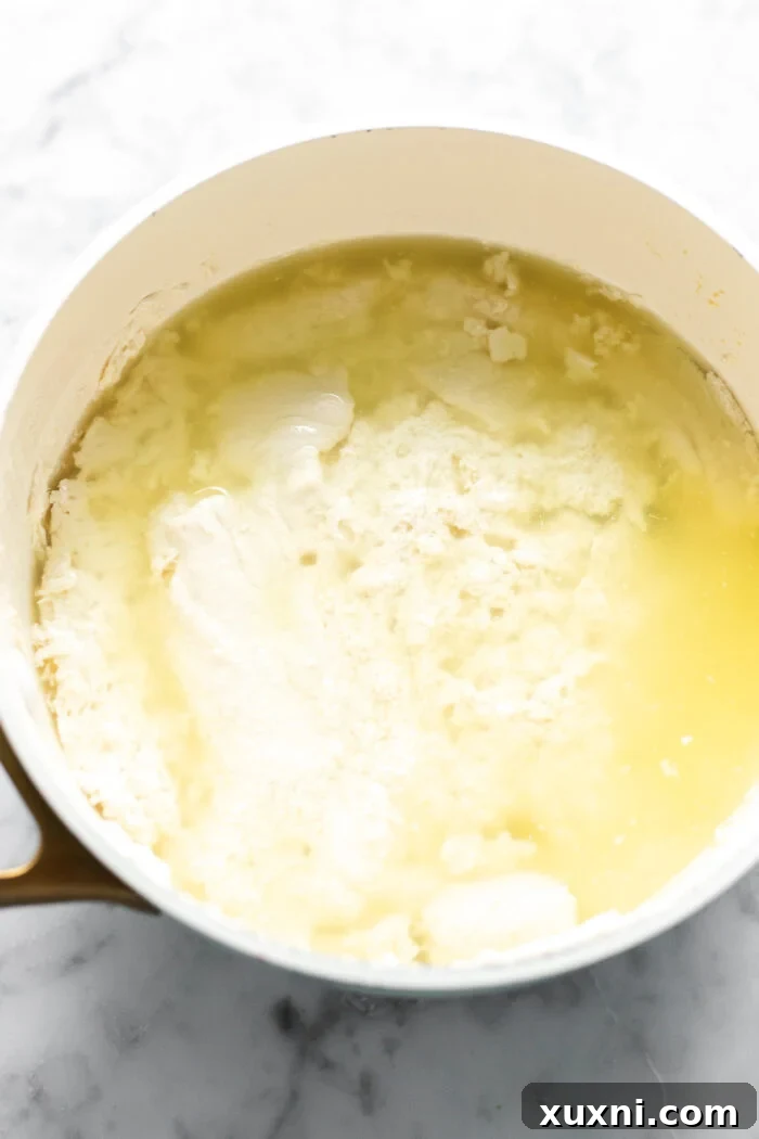 Pea milk and vinegar mixture coming to a boil in a saucepan, showing initial coagulation.