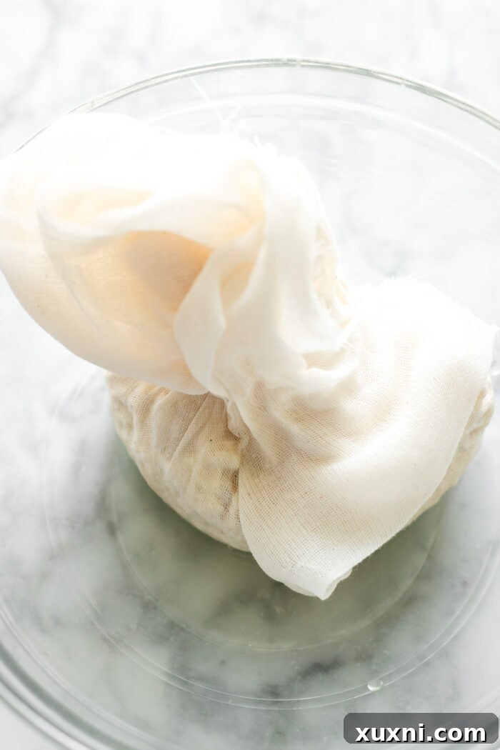 Straining the curdled pea milk mixture through cheesecloth into a bowl.