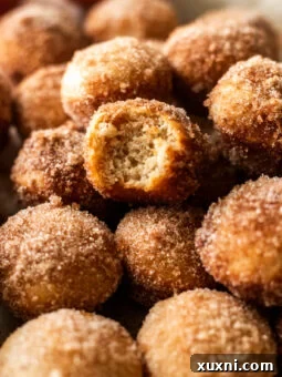 A close-up of a bitten vegan apple cider donut hole on a mound of other donut holes, illustrating its texture and appeal.