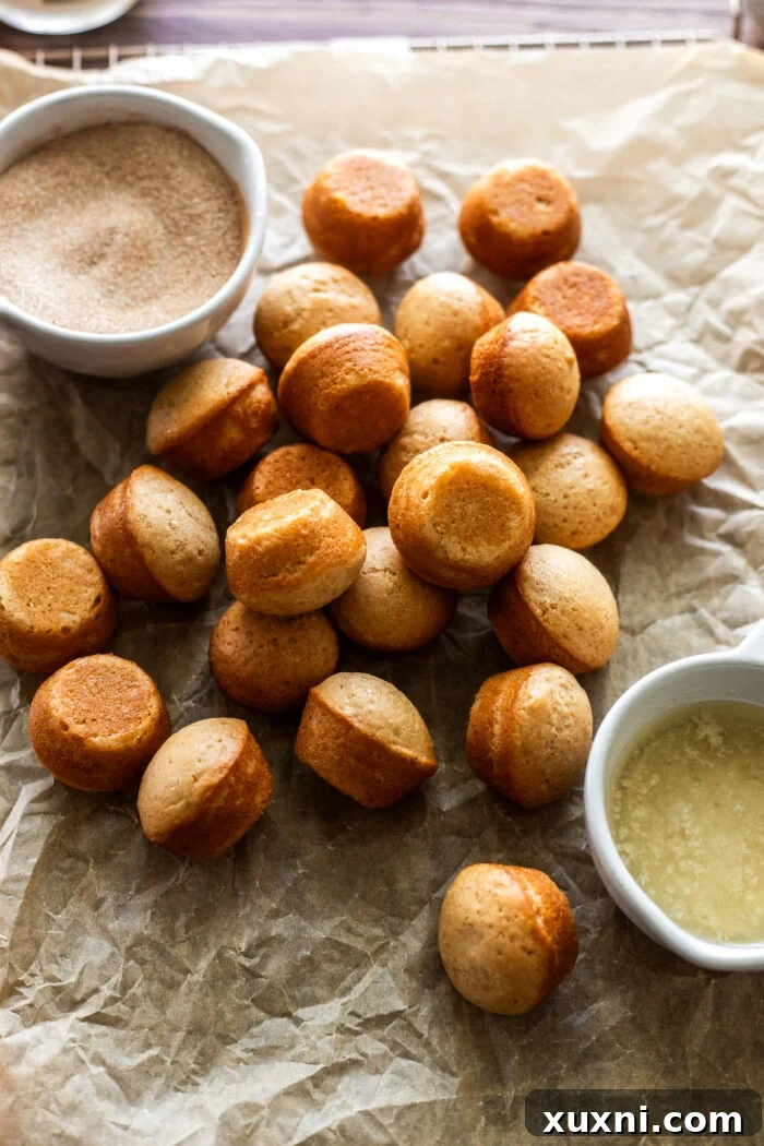 A baked donut hole being brushed with melted vegan butter.