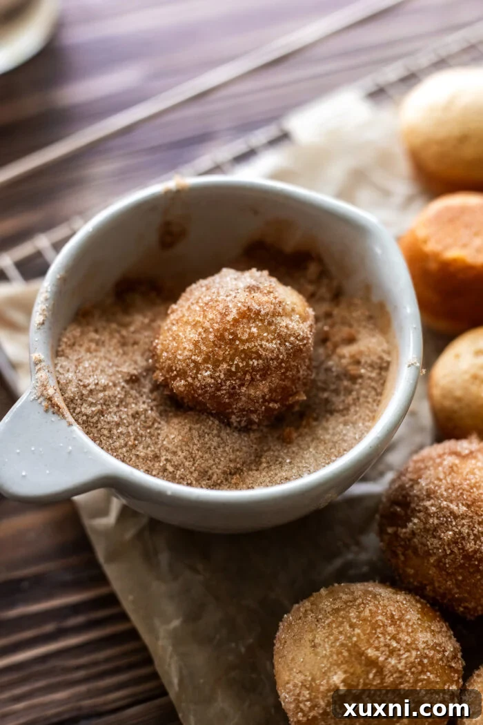 Donut holes being rolled in a bowl of cinnamon sugar.