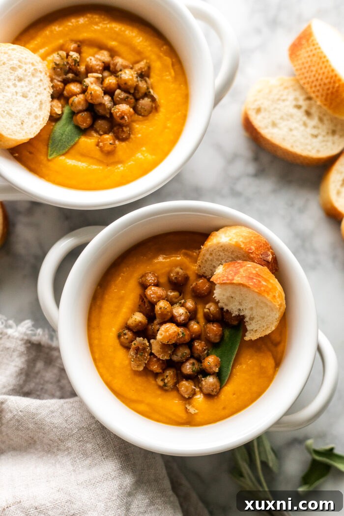 Two bowls of golden, creamy pumpkin soup served with crunchy bread slices and a scattering of fresh herbs, emphasizing its comforting appeal.
