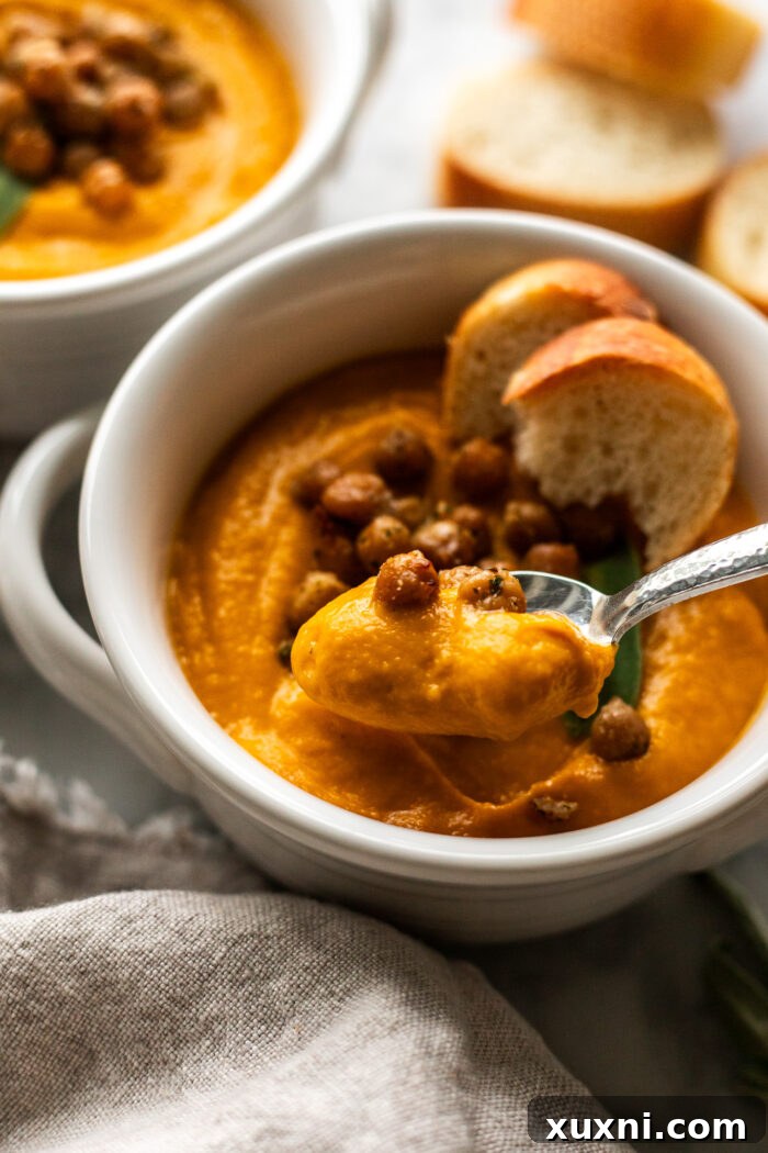 A spoon scooping a generous portion of creamy pumpkin soup from a bowl, highlighting its smooth, inviting texture.