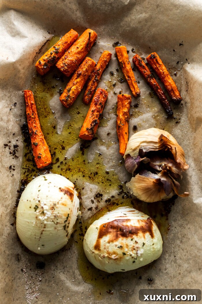 A baking sheet filled with an assortment of colorful roasted vegetables including pumpkin, carrots, onions, garlic, and chickpeas, seasoned and ready for the oven.