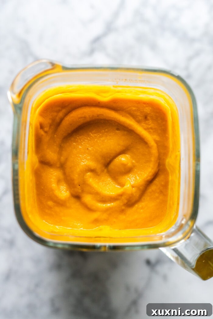 The smooth, vibrant orange texture of blended pumpkin soup filling a blender jar, indicating it's perfectly pureed.