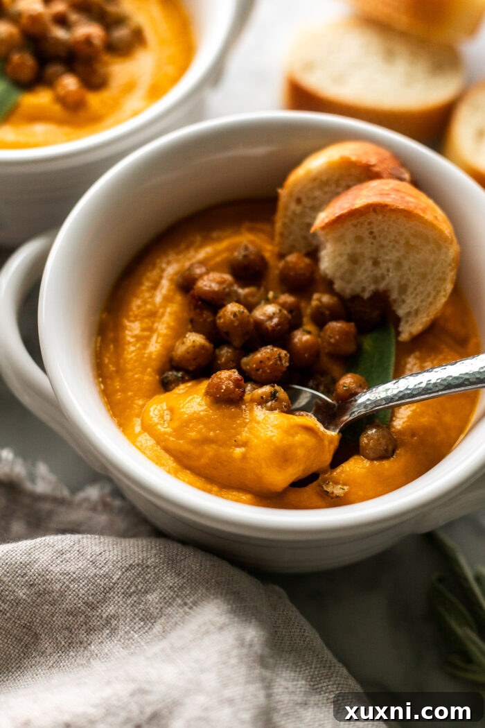 A comforting bowl of creamy vegan pumpkin soup topped with golden crispy chickpeas and a side of crusty bread, ready to be enjoyed as a meal.