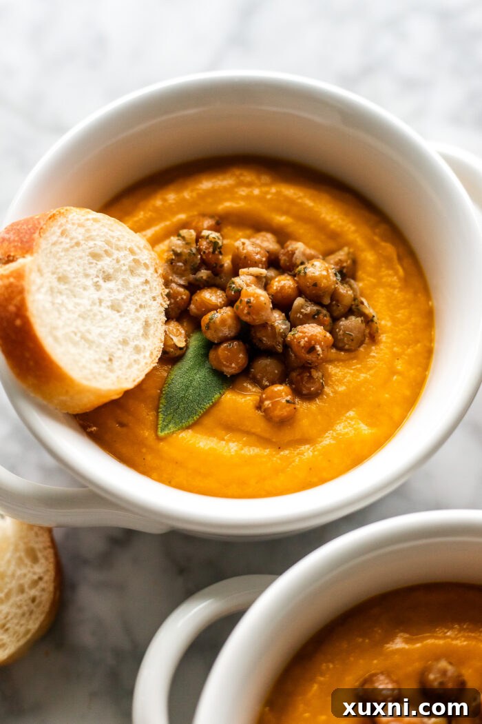 A close-up shot of a bowl of creamy pumpkin soup, generously topped with golden crispy chickpeas and served with thick slices of homemade garlic bread.