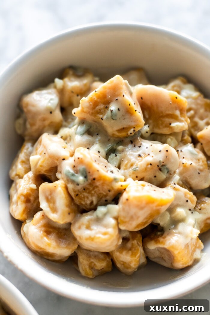 A beautifully plated bowl of vegan pumpkin gnocchi, garnished with fresh sage leaves and vegan parmesan cheese.